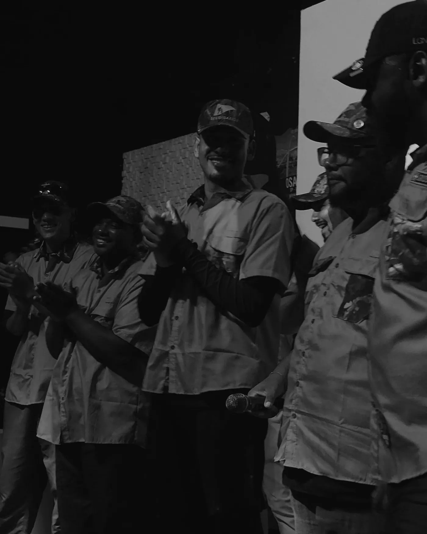 Legendários da HDF aplaudindo no palco, de camisa e boné do movimento.